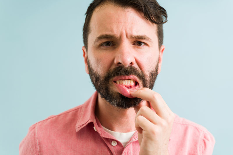 man with dental issues holding lip down, blue background